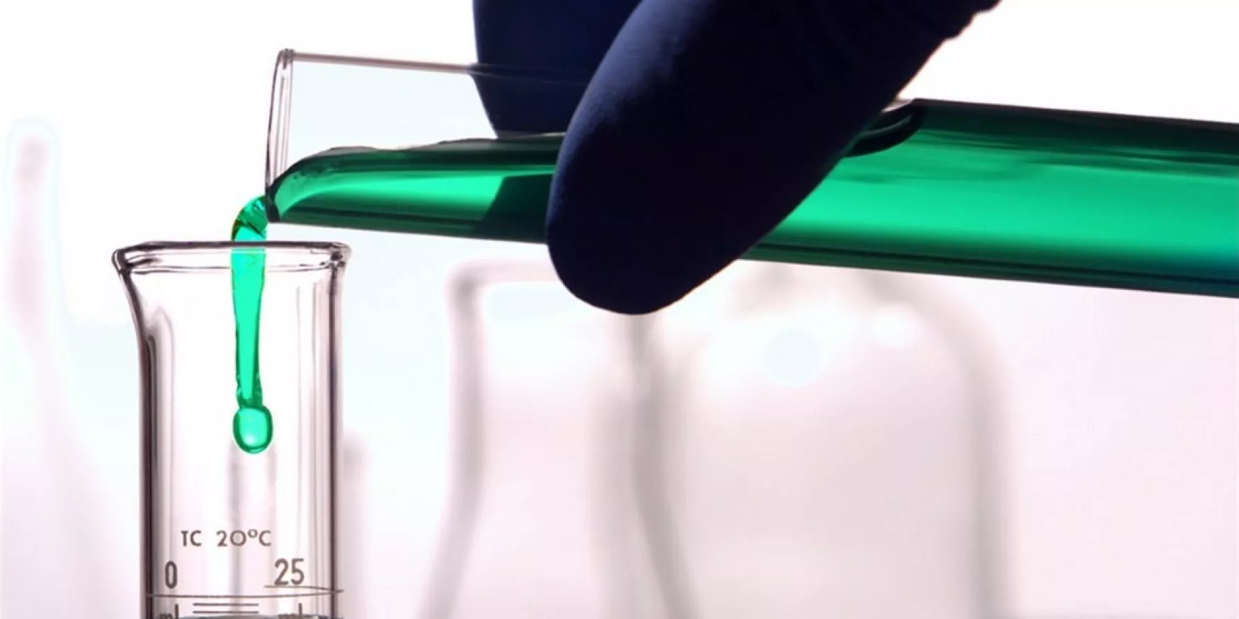 Expérience chimique où une main gantée verse un liquide dans un cylindre gradué ; Chemical experiment in which a gloved hand pours a liquid into a graduated cylinder ; Chemisches Experiment, bei dem eine behandschuhte Hand eine Flüssigkeit in einen Messzylinder gießt