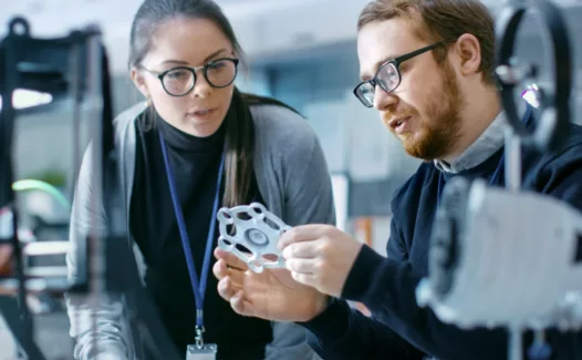 Deux ingénieurs dans un laboratoire discutant d'un prototype réalisé avec une imprimante 3D ; Two engineers in a laboratory discussing a prototype made using a 3D printer ; Zwei Ingenieure diskutieren in einem Labor über einen mit einem 3D-Drucker hergestellten Prototyp